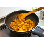 Une poêle remplie de poulet au curry épicé en train de cuire sur une cuisinière, présentant une riche teinte dorée