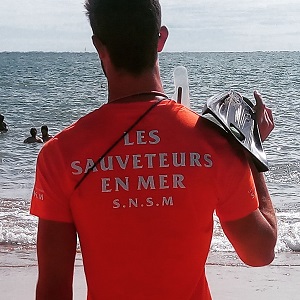 Homme sauveteur en mer en orange de dos avec ses palmes sur l'épaule