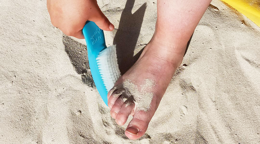 Brosse de plage bleu tenue à la main pour retirer le sable du pied