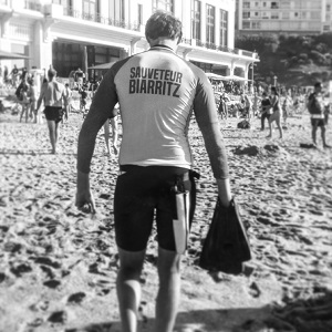 Homme sauveteur Biarritz qui marche sur la plage avec ses palmes dans la main droite