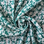 Tissu mousseline polyester fleuri blanc effet froissé sur fond vert.