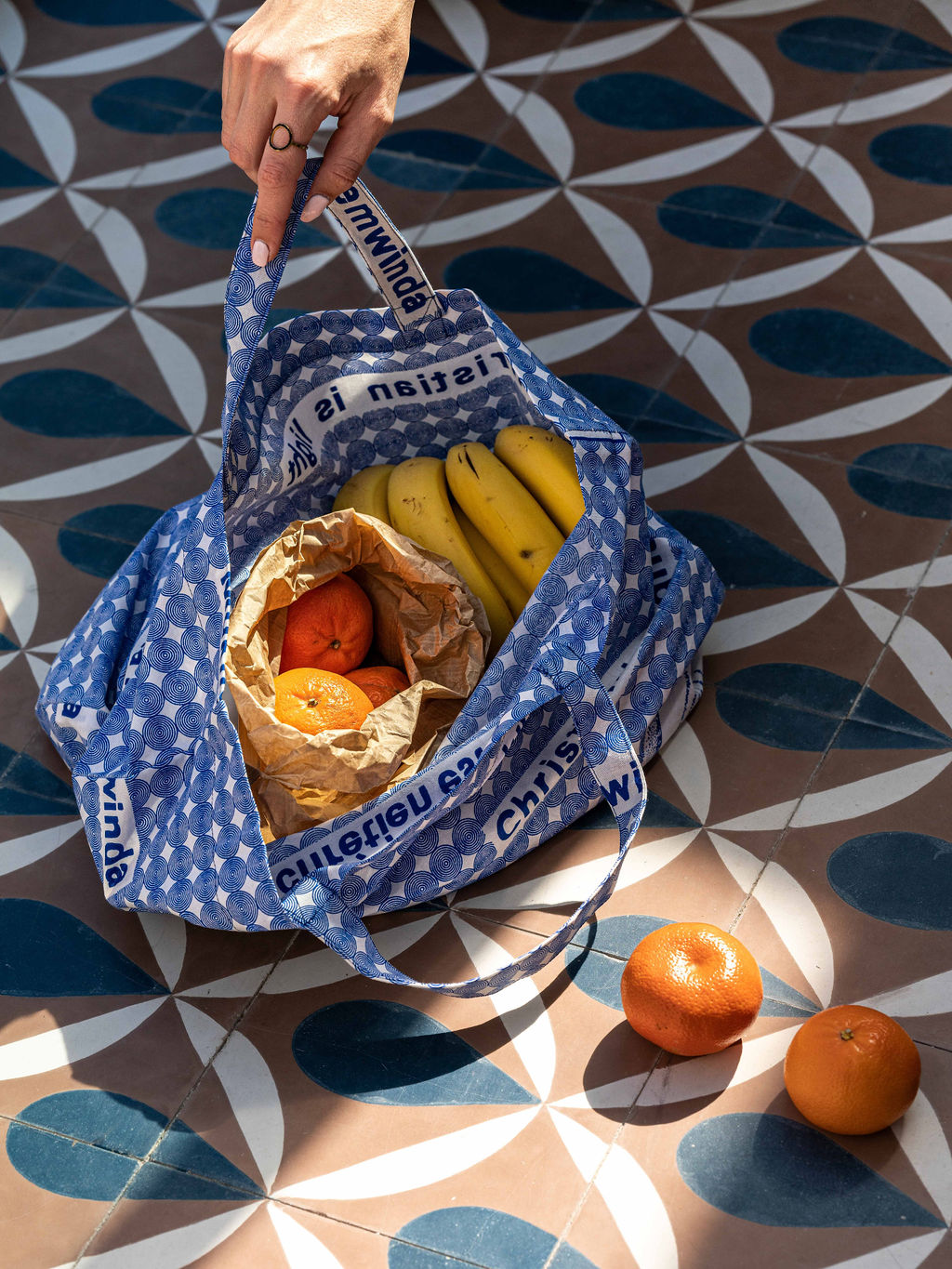 une main de femme tient un sac bleu pose au sol et rempli de fruits