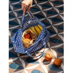 une main de femme tient un sac bleu posé au sol et rempli de fruits