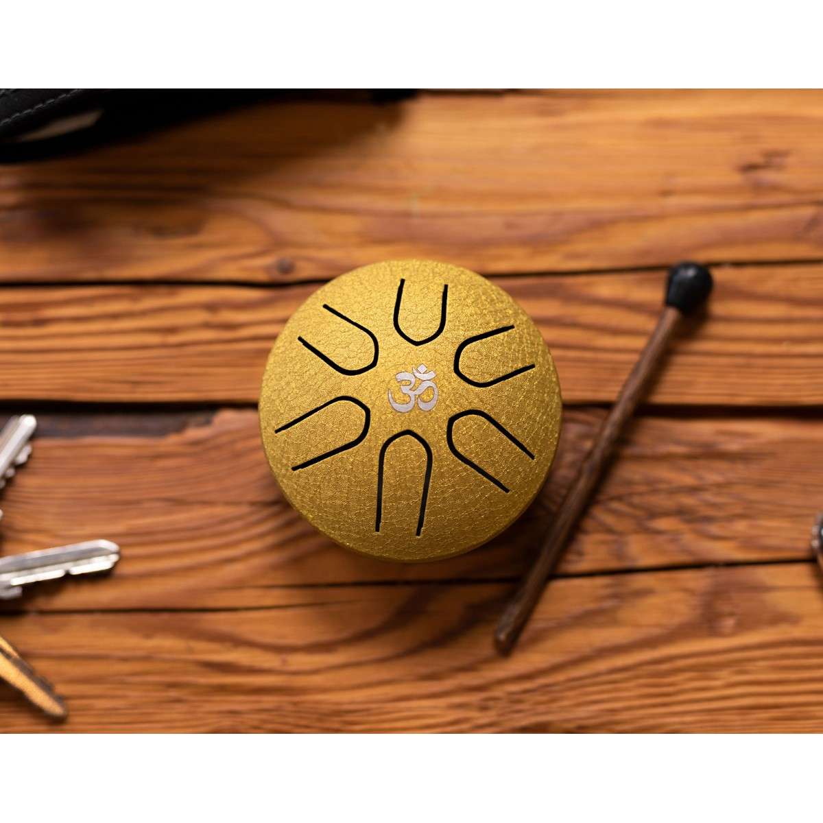 Tongue drum en acier doré Meinl posé sur une table en bois avec maillet de jeu et trousseau de clés.