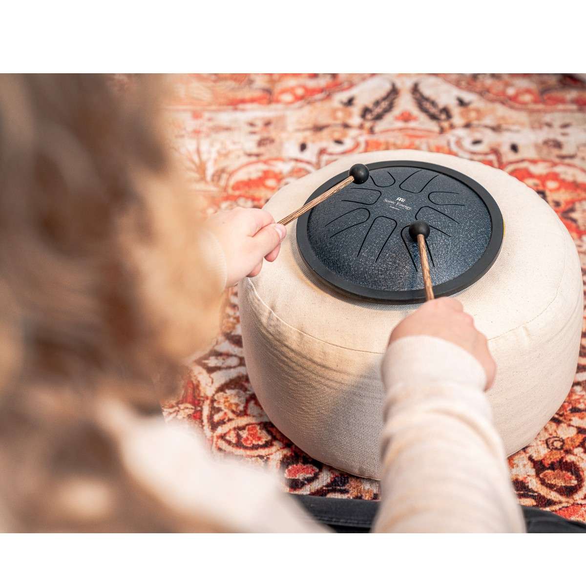 Enfant jouant du mini steel tongue drum Meinl en Sol mineur bleu avec maillets sur coussin de méditation