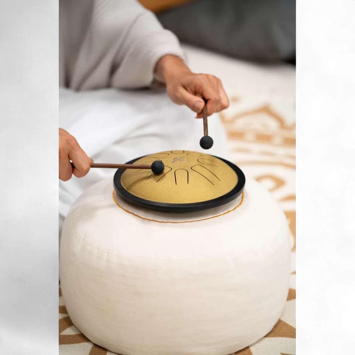 Vue plongeante sur le mini tongue drum doré joué avec maillets sur coussin rond