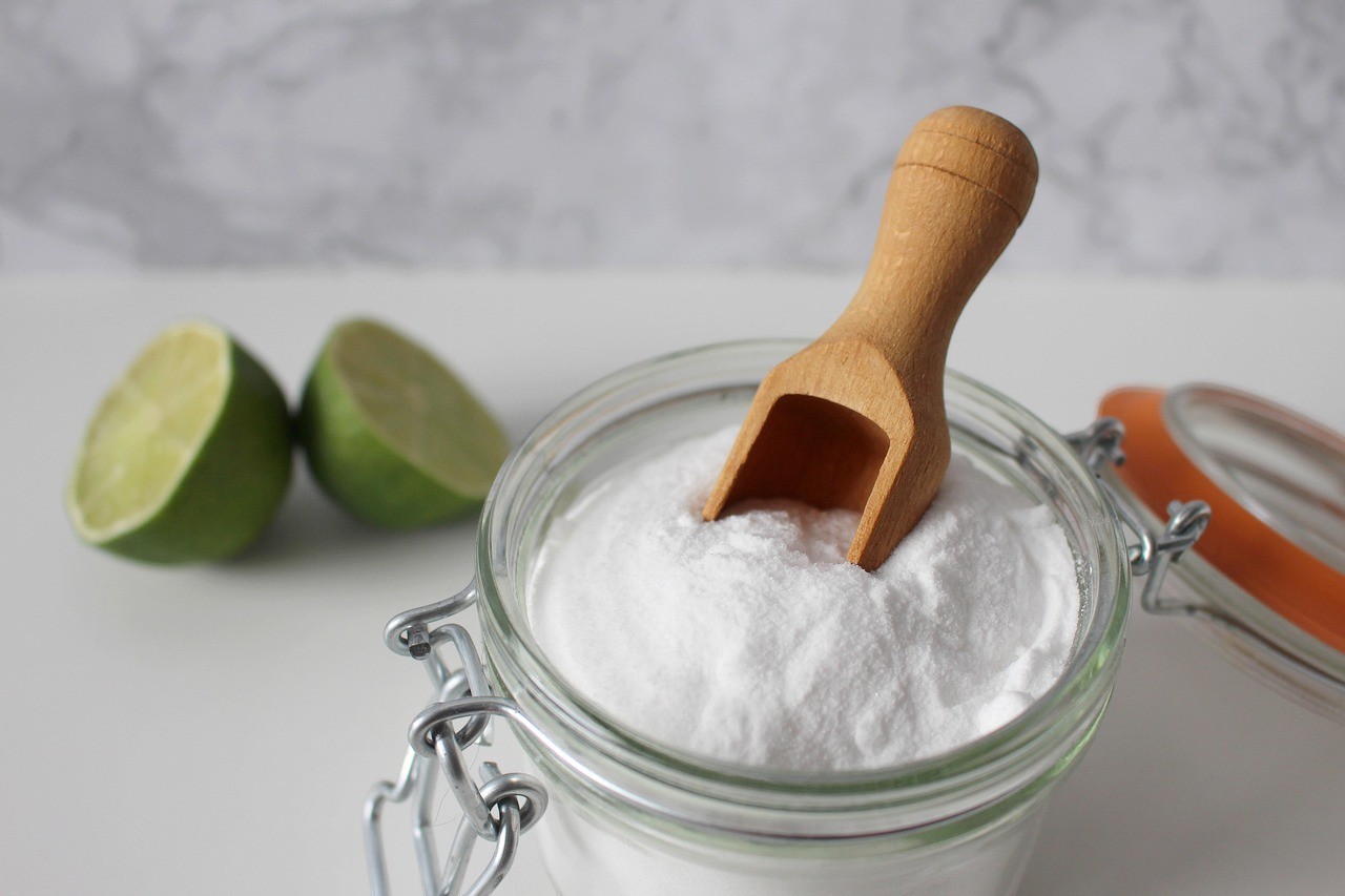 Bicarbonate de soude alimentaire dans un bocal ouvert avec deux citrons coupés, utilisé pour préparer une eau alcaline maison