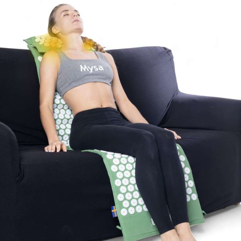 Femme assise sur un canapé avec le tapis Mysa le long du dos et le coussin chauffant sous les cervicales