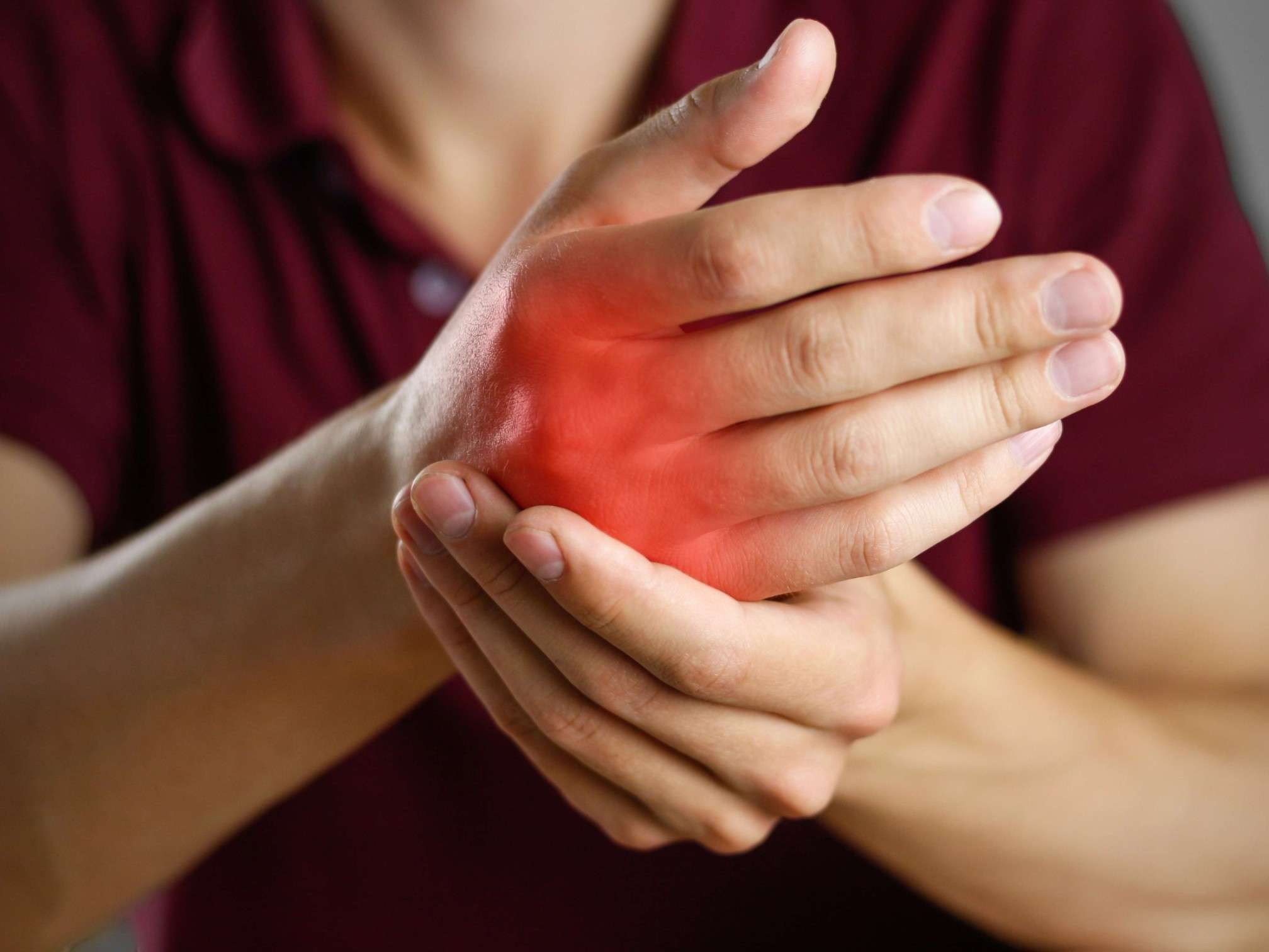 Personne tenant sa main douloureuse avec une zone rouge, illustration de douleur articulaire liée à l’arthrose