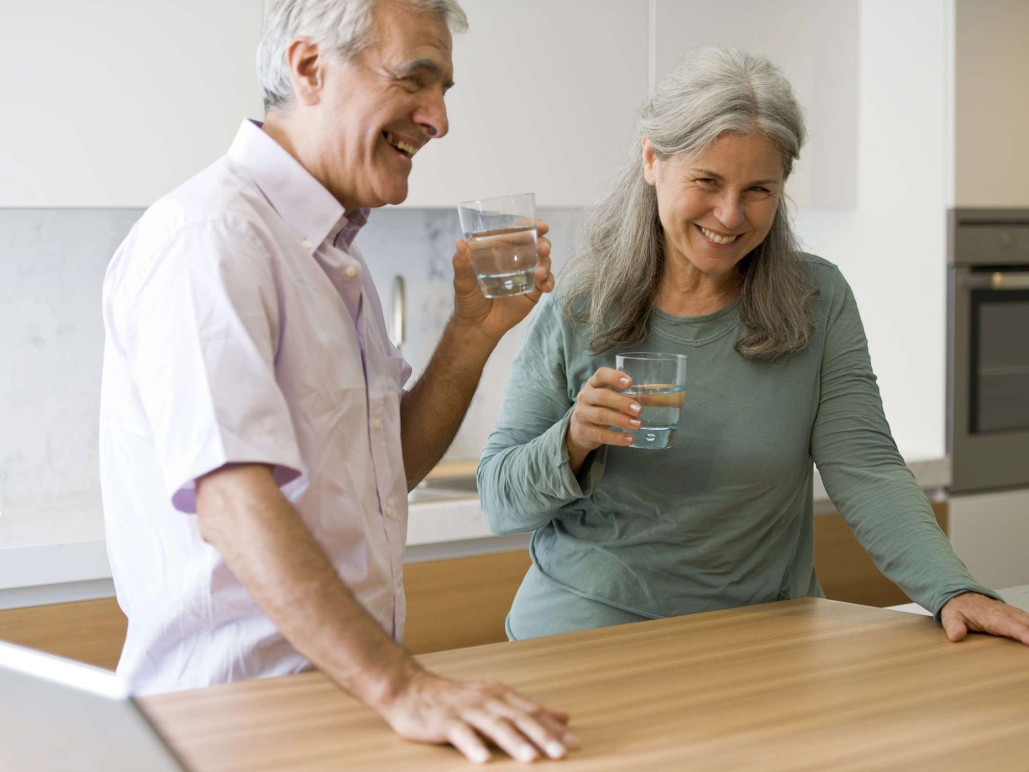 Couple de seniors souriants buvant un verre d’eau dans la cuisine, hydratation et bien-être articulaire