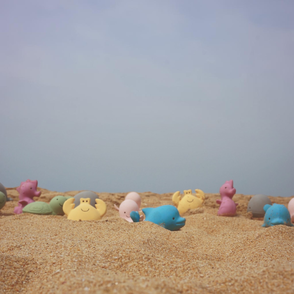 Collection de jouets marins Tikiri en caoutchouc naturel dispersés sur une plage de sable