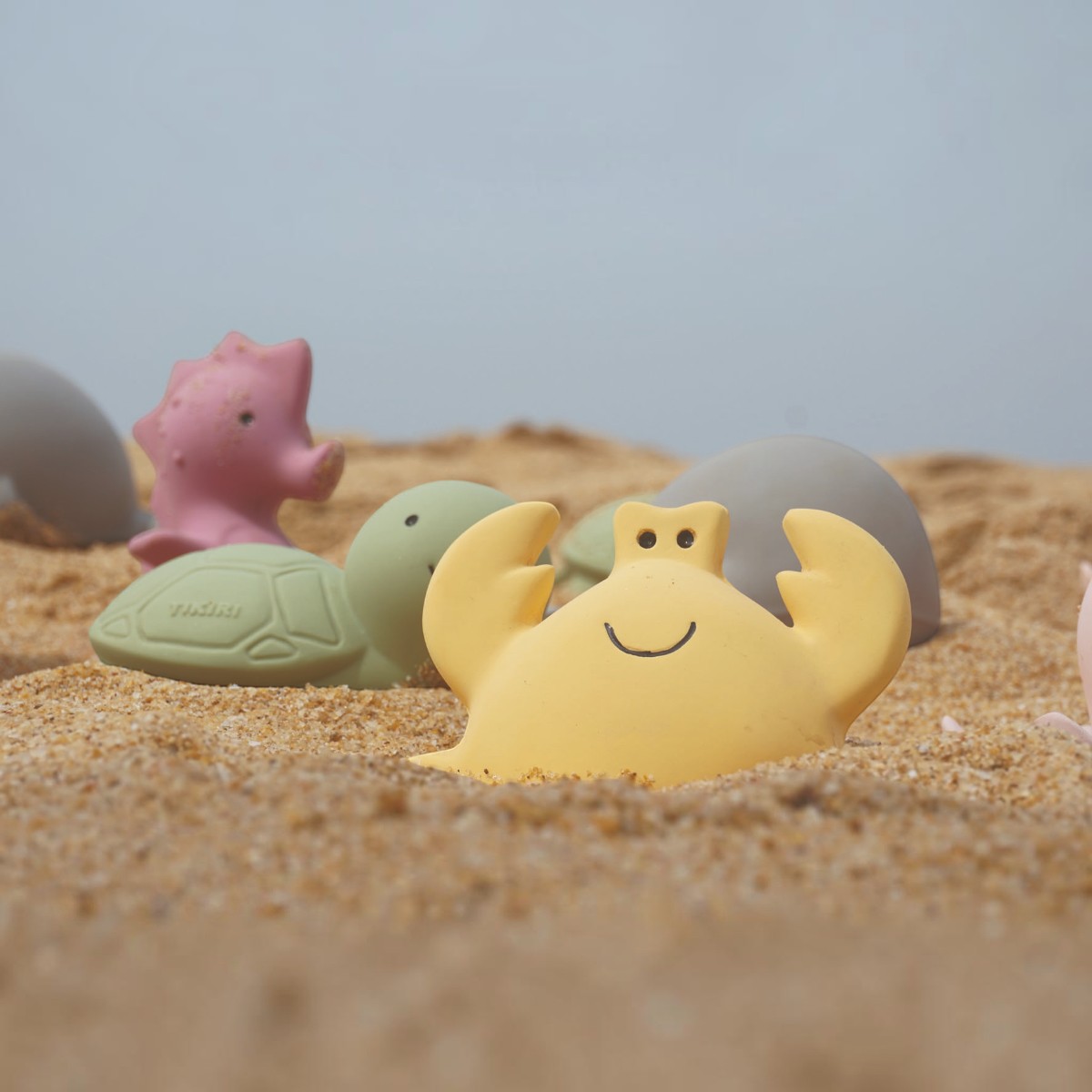 Crabe jaune Tikiri en caoutchouc naturel posé dans le sable, tortue et hippocampe en arrière-plan