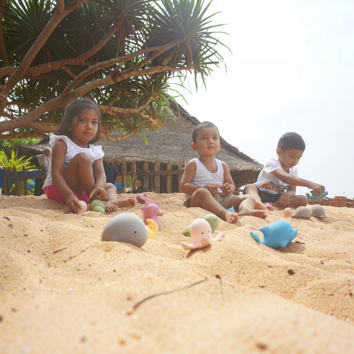 Trois enfants jouant sur le sable avec les jouets Tikiri baleine, hippocampe, poulpe et dauphin