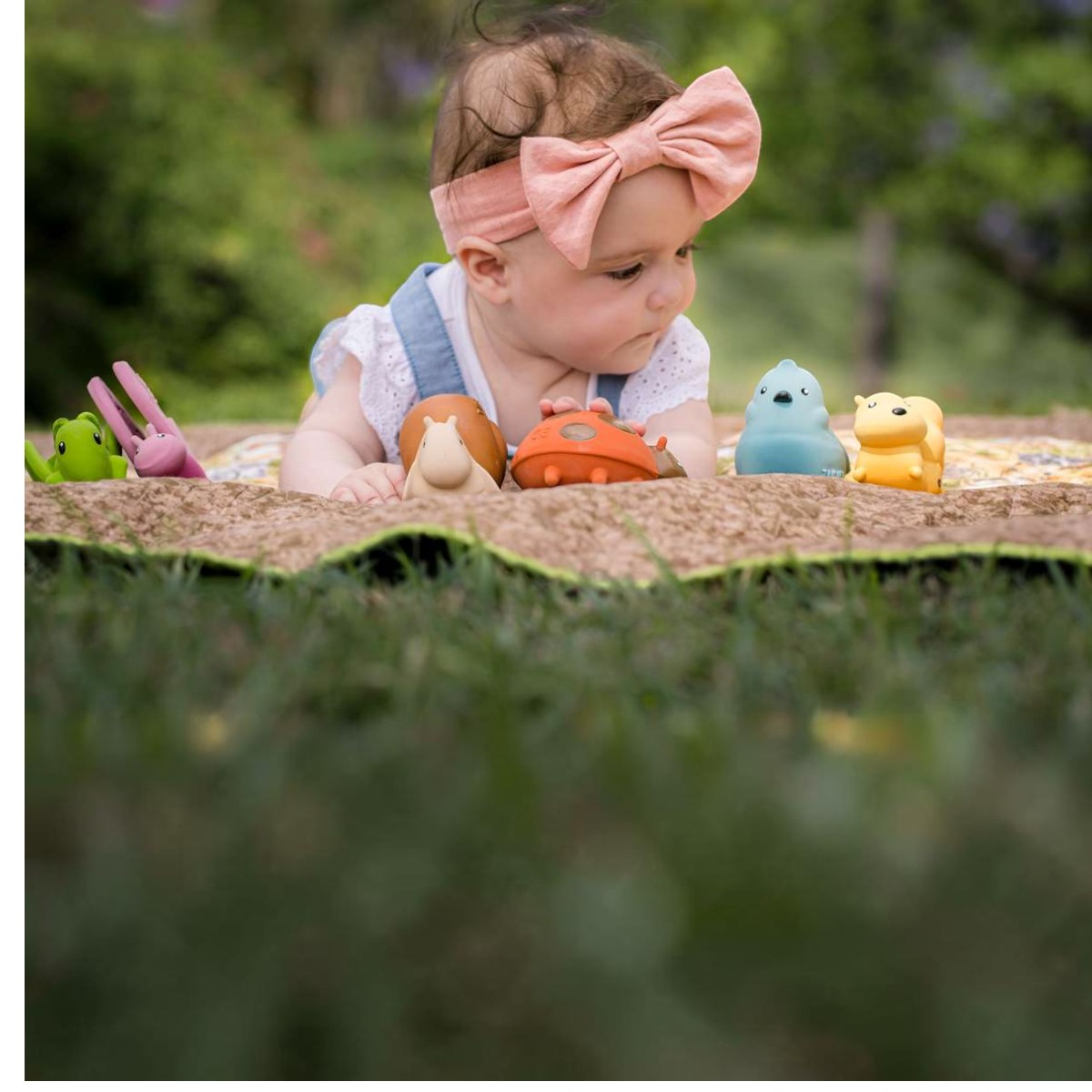 Bébé allongée sur un plaid dans lherbe, devant les six petites bêtes du jardin Tikiri en caoutchouc naturel