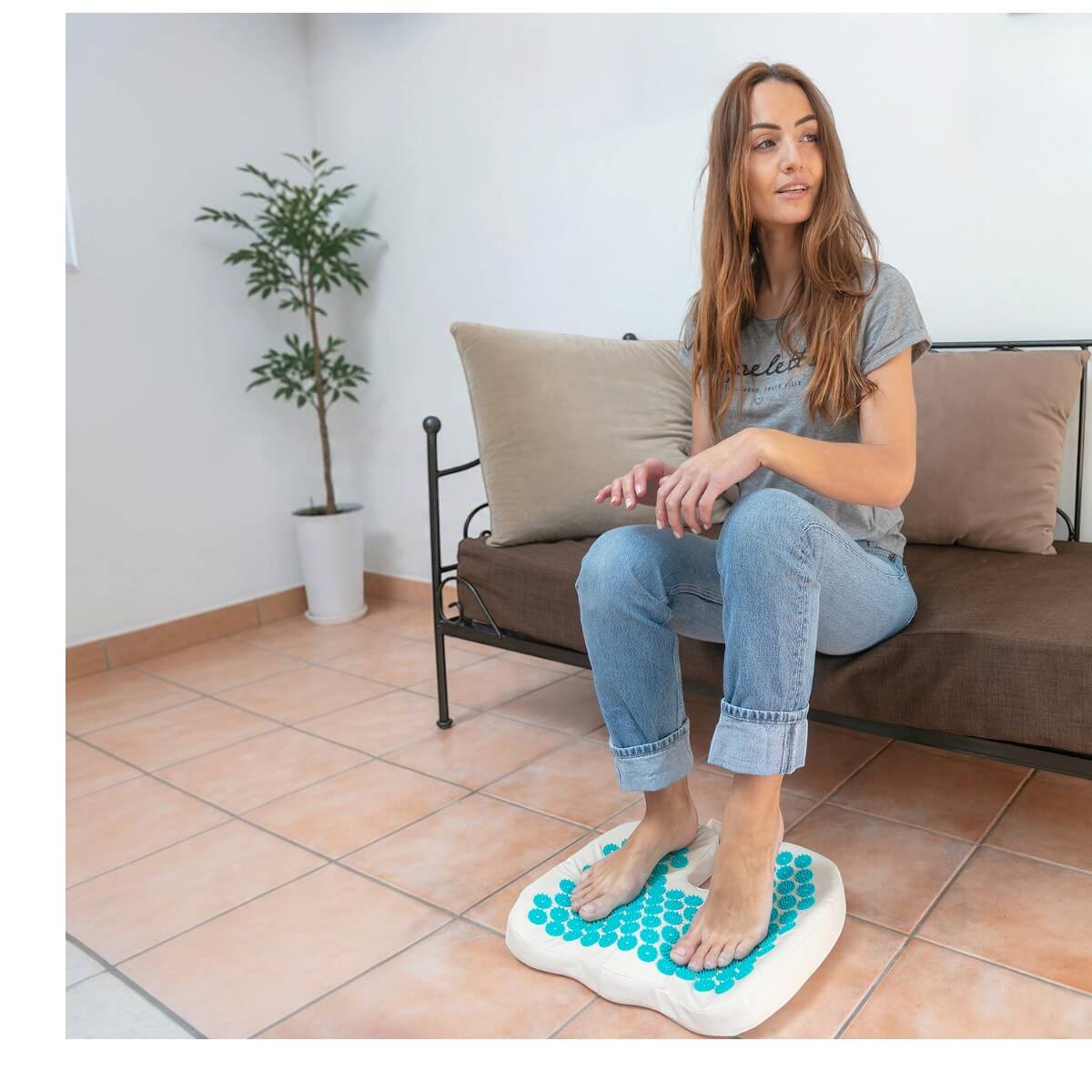Femme assise sur un canapé, pieds nus sur le coussin d’acupression pour les pieds Climsom Zen