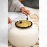 Vue plongeante sur le mini tongue drum doré joué avec maillets sur coussin rond