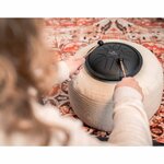 Personne jouant du mini steel tongue drum Meinl noir avec des maillets, posé sur un coussin rond beige