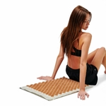 Femme assise sur le tapis d’acupression Akumata Eco avec pointes dorées