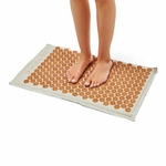 Personne debout sur le tapis d’acupression Akumata Eco aux pointes dorées