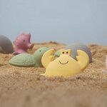 Crabe jaune Tikiri en caoutchouc naturel posé dans le sable, tortue et hippocampe en arrière-plan