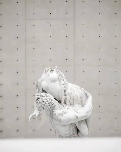 Sculpture monumentale en cire d'Urs Fischer en train de se consumer lors d'une exposition d'art moderne.
