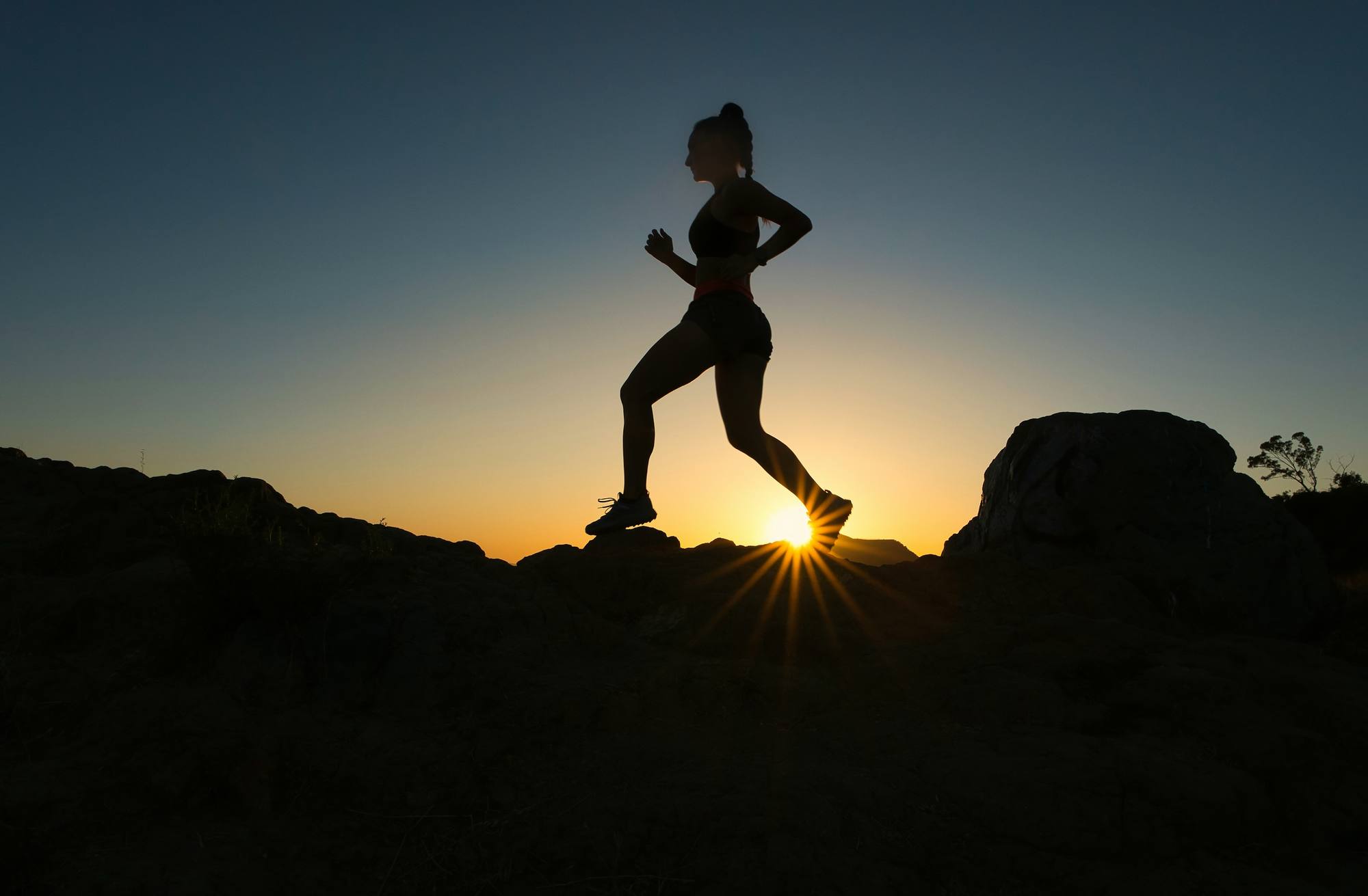 Silhouette d'une traileuse qui court sur les rochers au coucher du soleil
