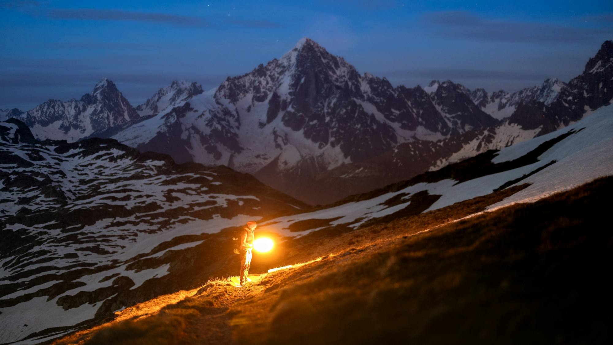 Frontale allumée sur un sentier de montagne à la nuit tombée, face aux glaciers