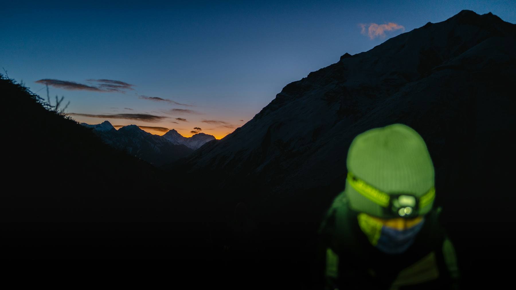 Traileur équipé d'une frontale allumée au crépuscule, en montagne