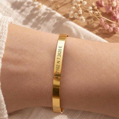 Bracelet jonc doré gravé de coordonnées GPS porté au poignet