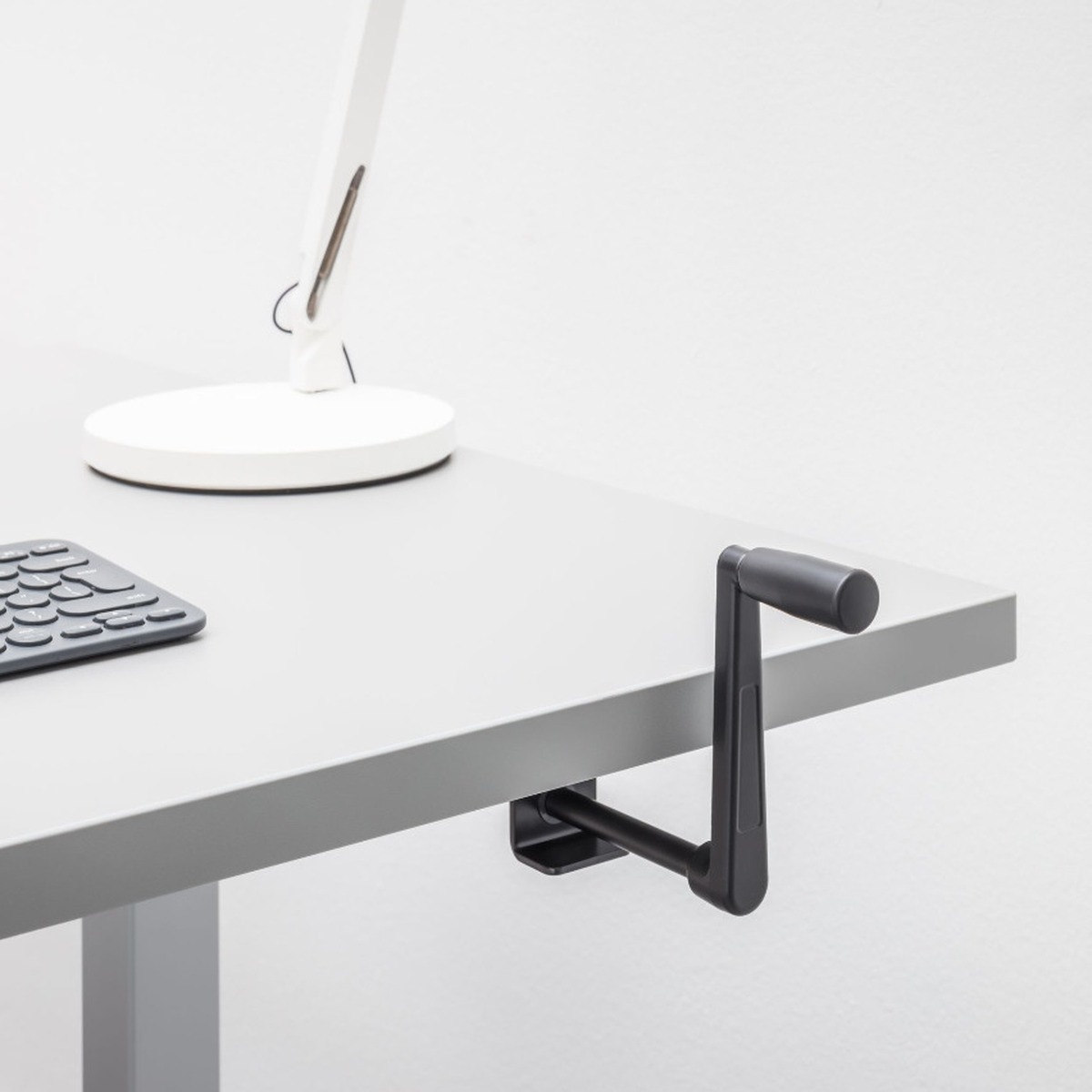 Détail de la manivelle rétractable noire fixée sous le plateau gris dun bureau bench Ogi Drive Bench