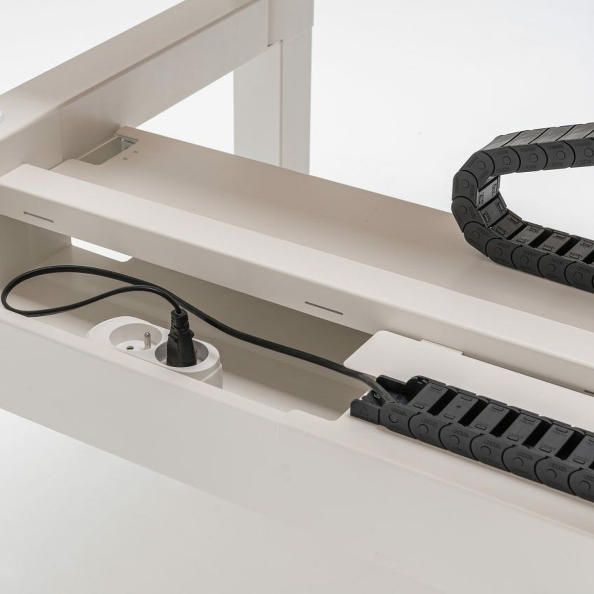 Détail du chemin de câbles partagé dun bench Ogi Drive blanc avec prise et chaîne porte-câbles