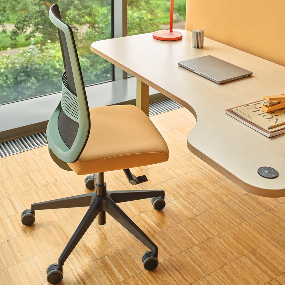 Chaise de bureau résille à coque vert sauge et assise ocre, vue de trois quarts devant une baie vitrée