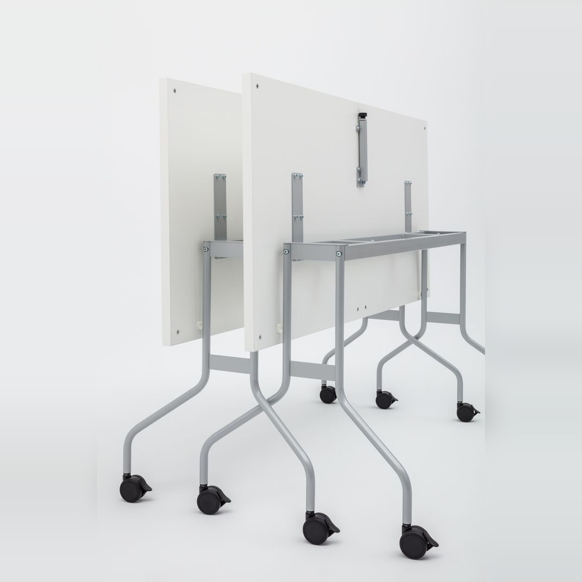Deux tables Easy à plateau blanc rabattues à la verticale, piétement gris sur roulettes, vue arrière