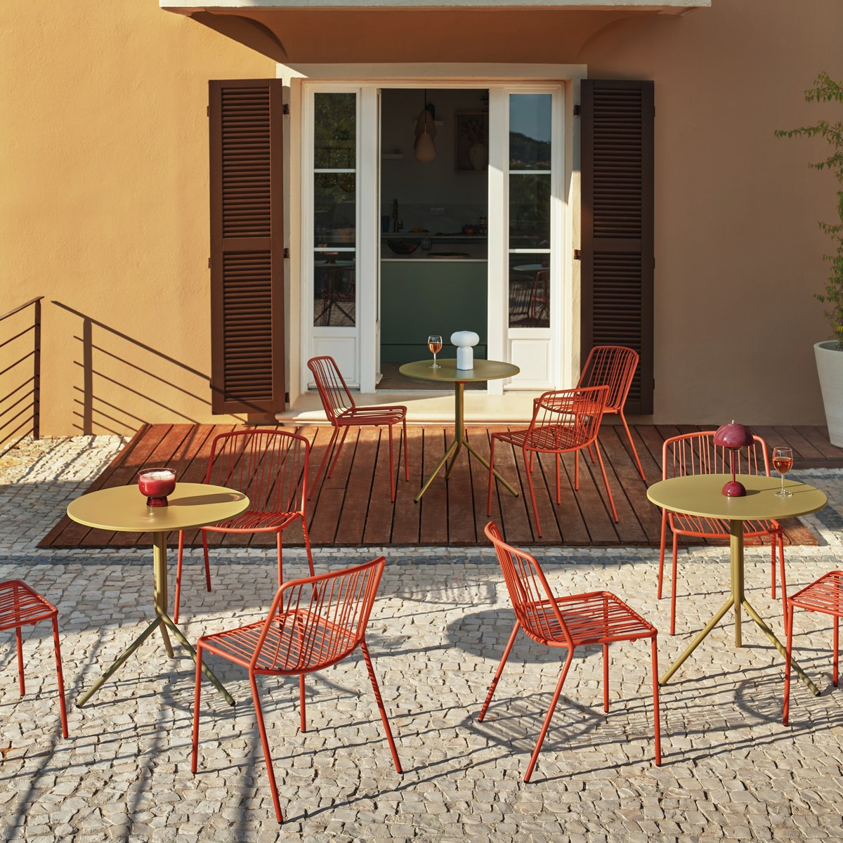 Terrasse avec trois tables de café Luna vert olive entourées de chaises métalliques orange