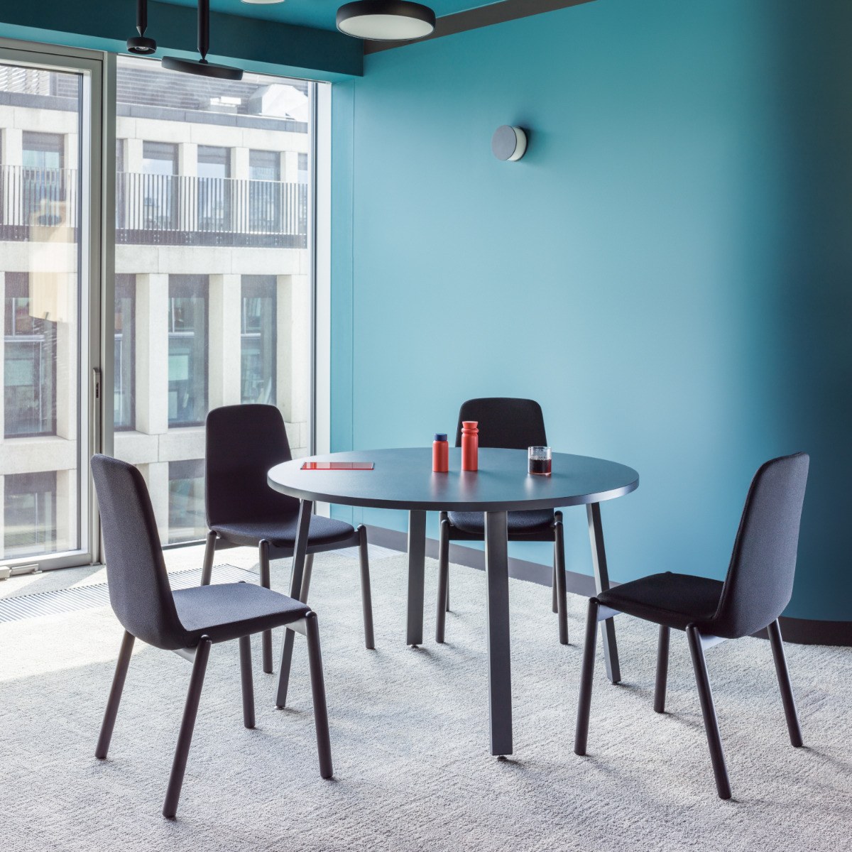 Table ronde Ogi A anthracite sur quatre pieds inclinés entourée de quatre chaises noires