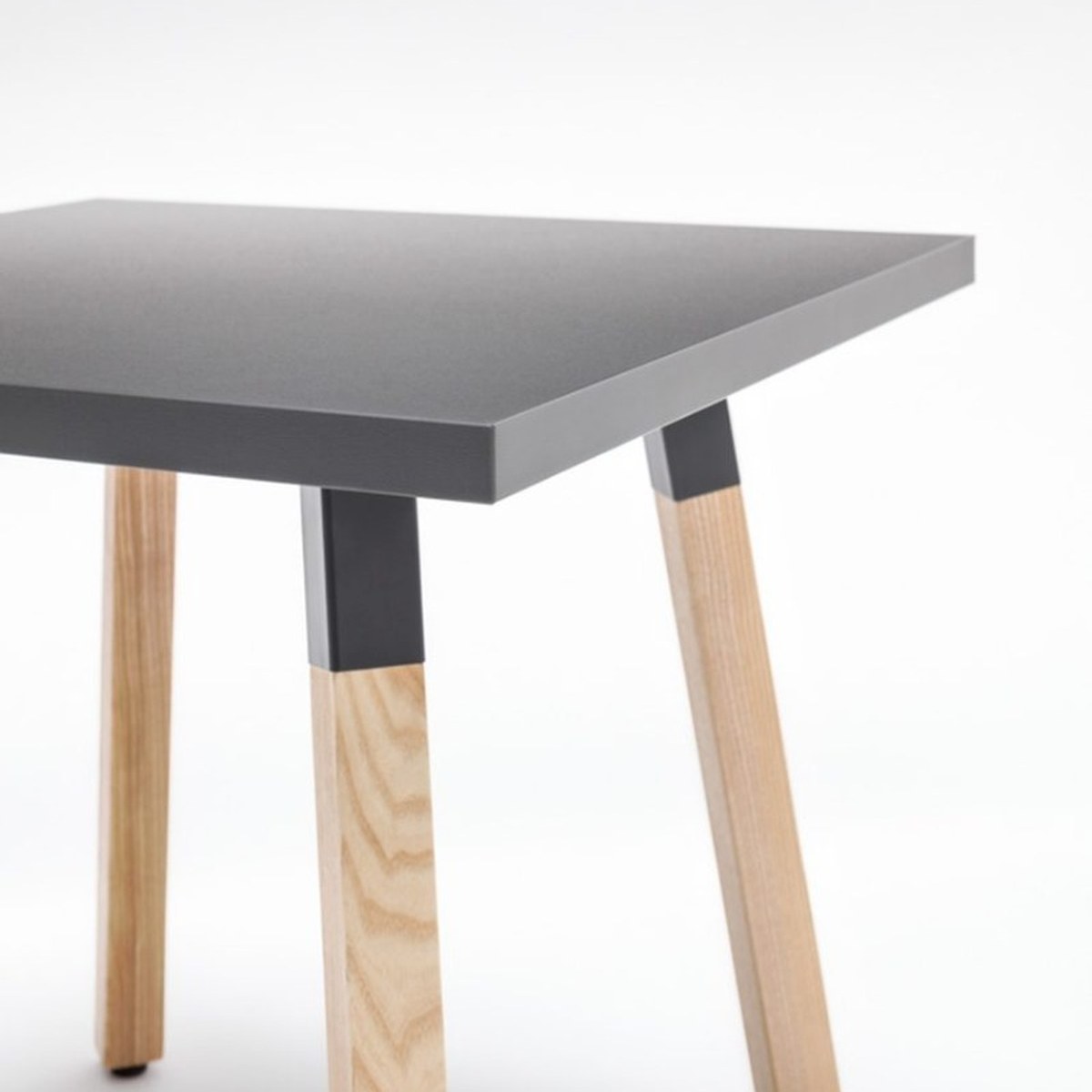 Détail dun angle de la table carrée Ogi W : manchon métallique noir emboîté sur un pied en frêne