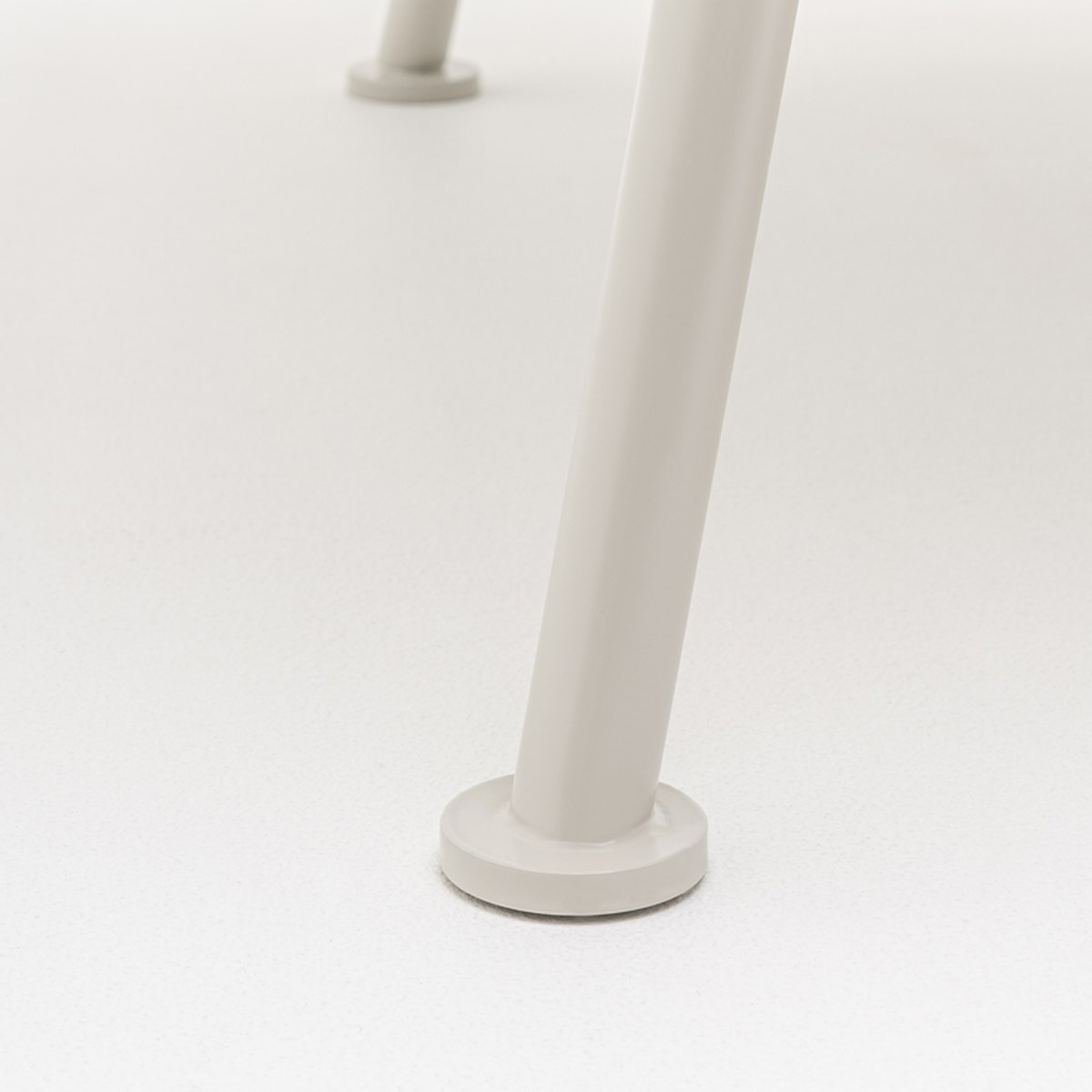 Détail dun pied en tube métal gris clair de la table New School et de son vérin de réglage