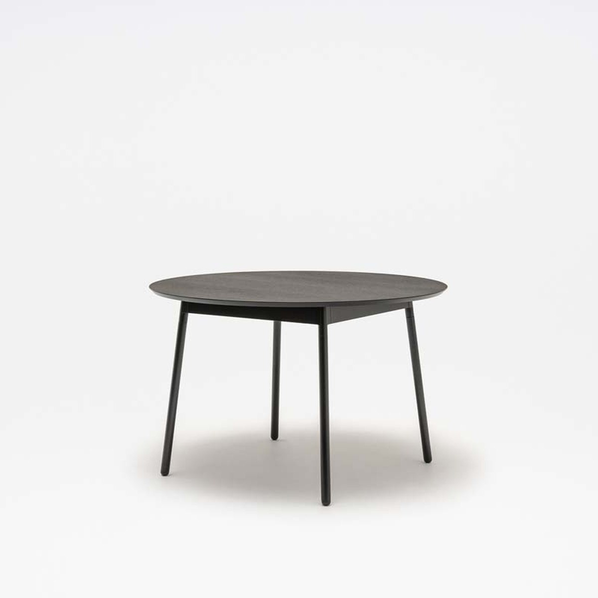 Table ronde Unit plateau chêne noir et piètement noir, vue de trois quarts sur fond gris clair