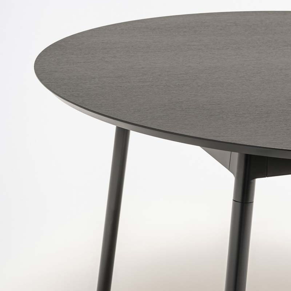 Vue rapprochée du plateau rond chêne noir de la table Unit et de ses pieds en tube Ø 35 mm