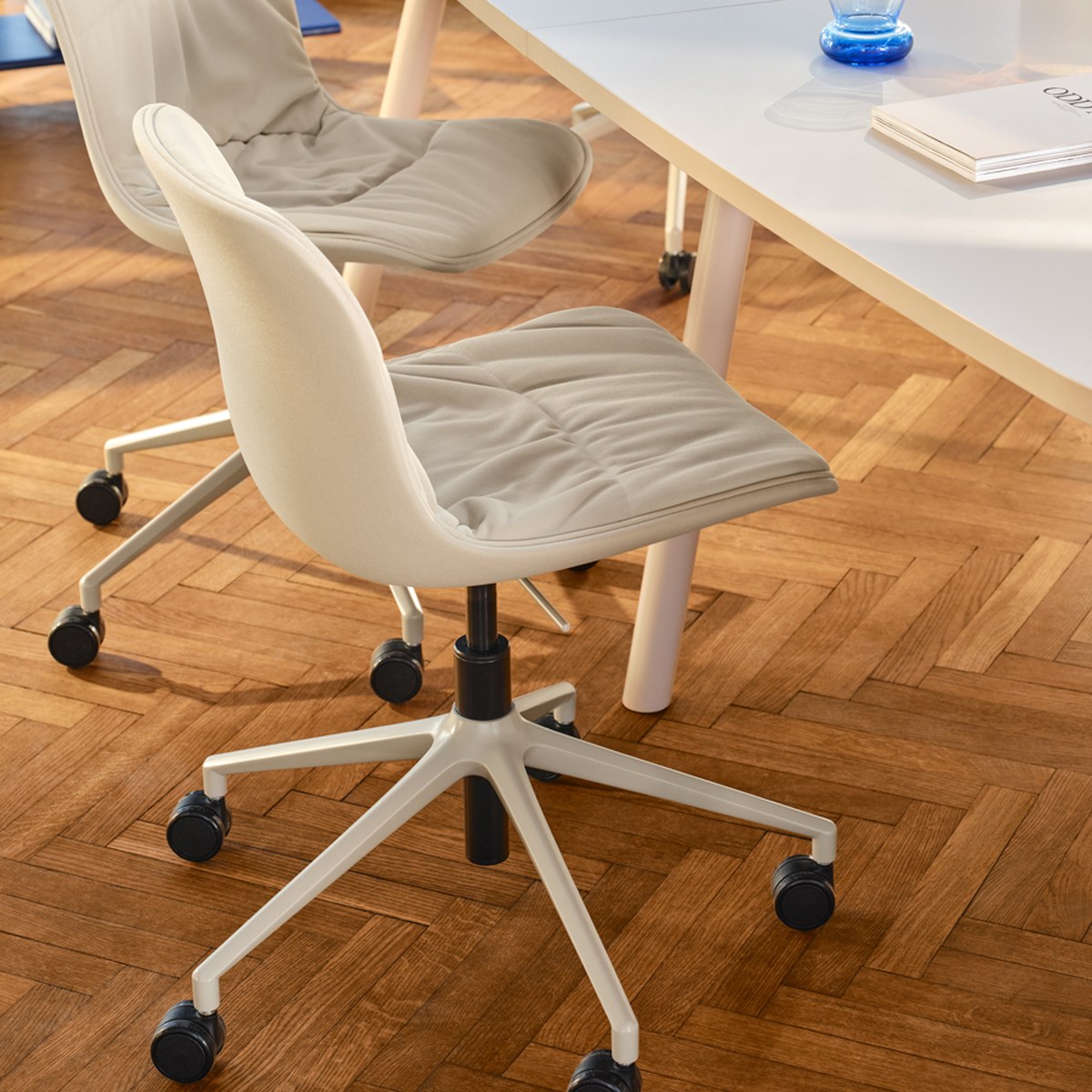 Chaise de bureau Baltic 2 Soft Duo blanche à roulettes devant une table de réunion