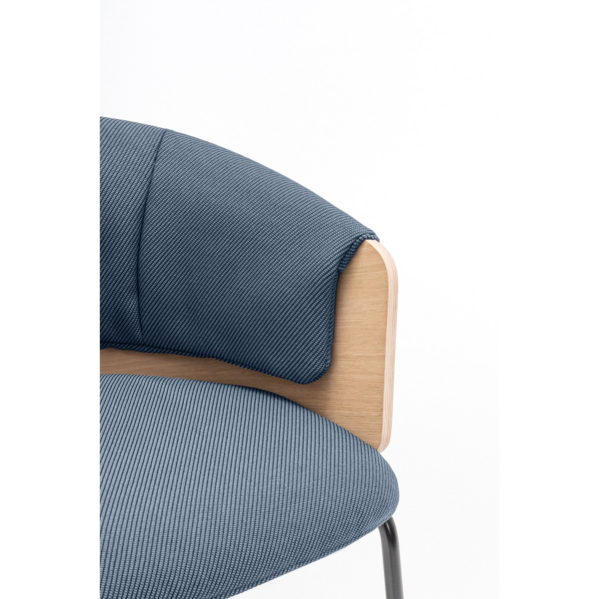Détail du coussin plissé bleu et du flanc en placage chêne de la chaise de réunion