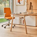 Chaise de bureau tapissée orange à piétement clair, devant un bureau en bois près d'une fenêtre