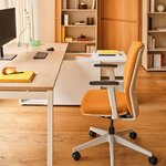 Chaise de bureau tapissée orange avec accoudoirs, vue rapprochée devant un bureau en bois clair