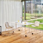 Table de réunion Revi blanche rabattable sur roulettes devant une baie vitrée, entourée de chaises claires