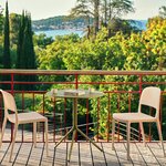 Table de café ronde Luna vert olive sur un balcon avec deux chaises claires et vue sur la mer