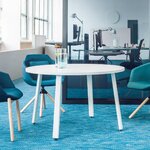 Table ronde Ogi A blanche à pieds blancs inclinés entre des fauteuils bleus dans un open space