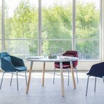 Table ronde Ogi W à quatre pieds en frêne et plateau clair, entourée de fauteuils bleus et bordeaux