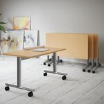 Table abattante plateau hêtre sur roulettes devant trois tables pliées et imbriquées, piétement aluminium
