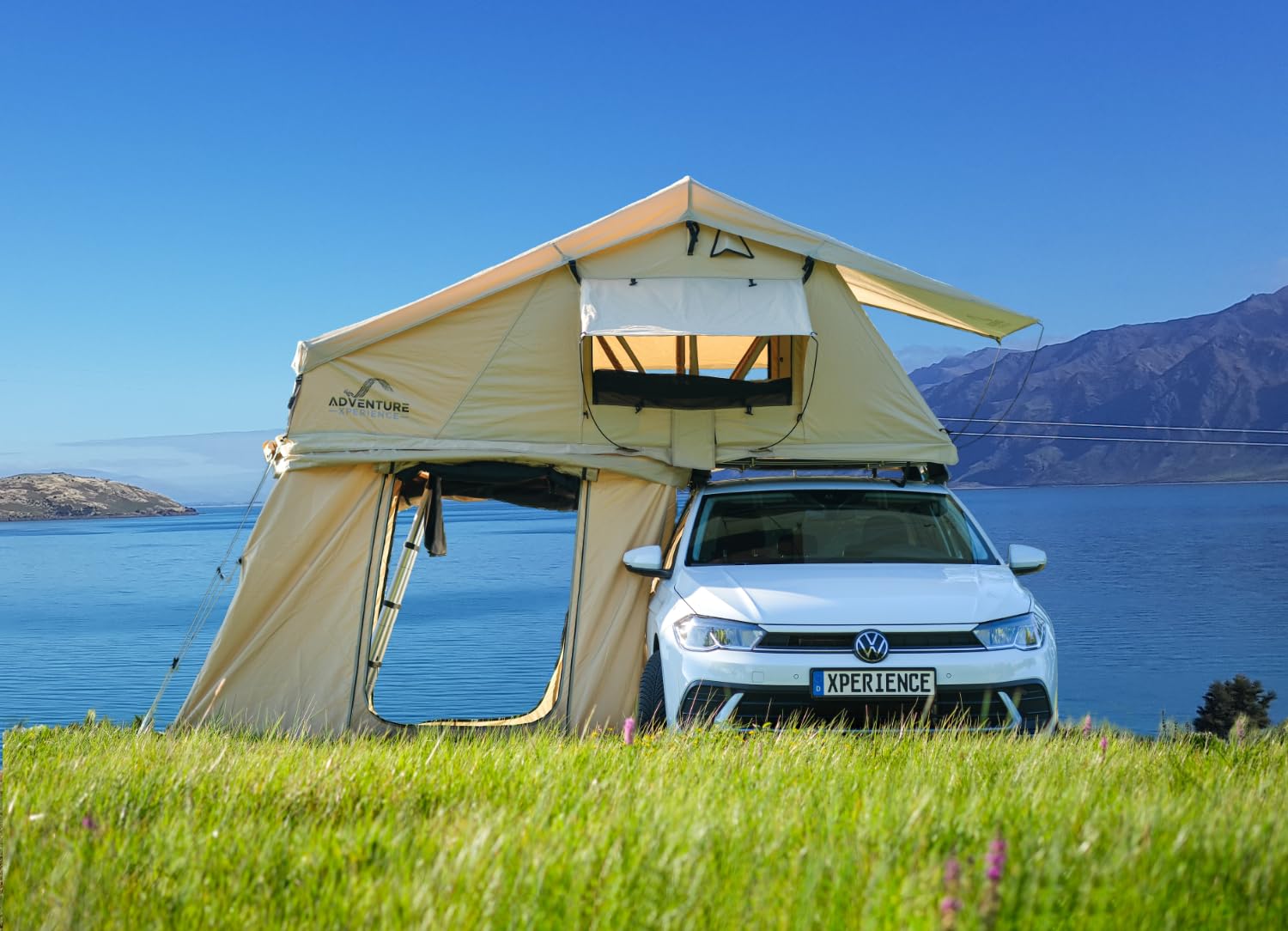 Tente de toit Adventure Xperience 140 ouverte avec son auvent sur une citadine, au bord d’un lac