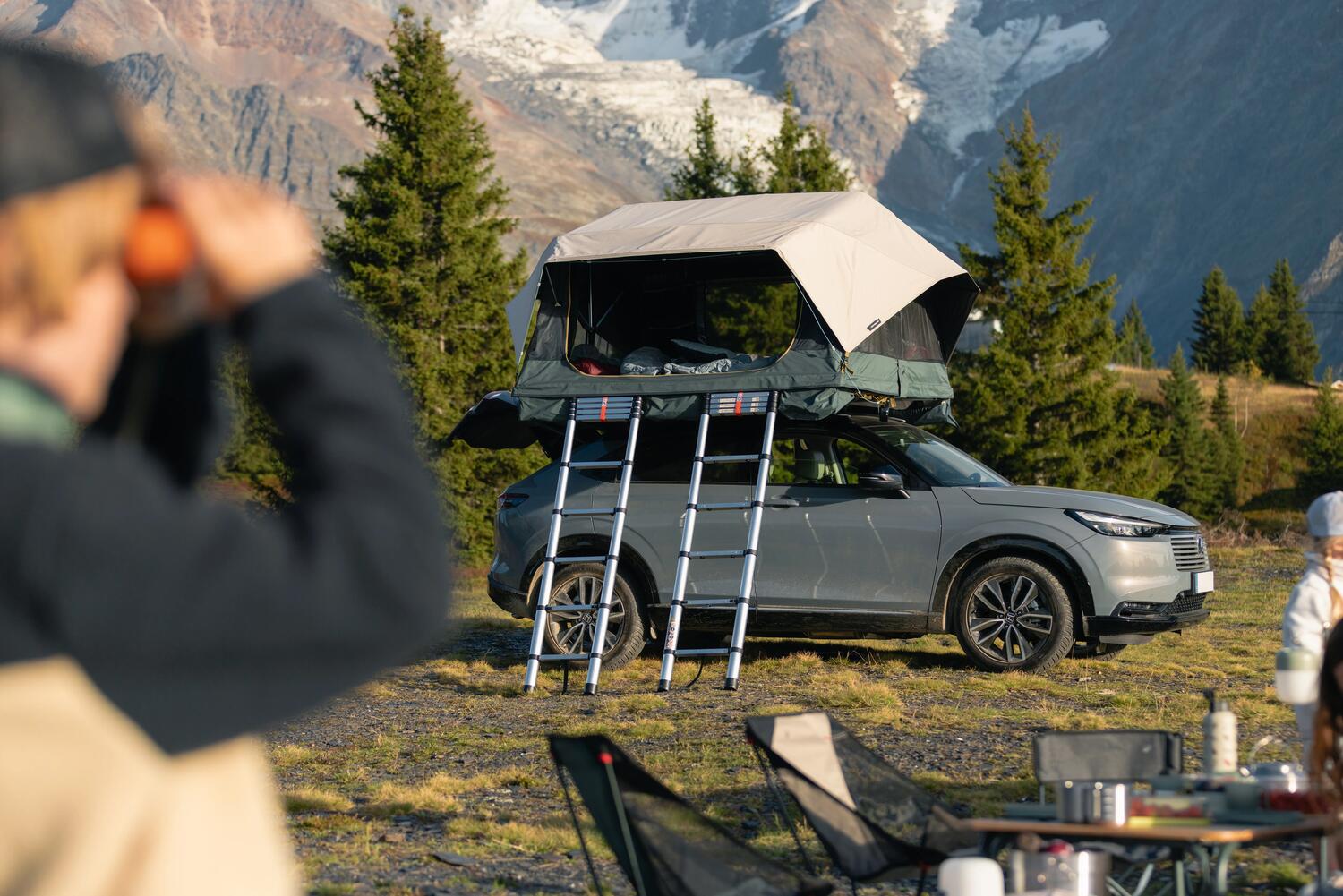 Tente de toit 500 4P Family ouverte sur un SUV gris, campement en montagne